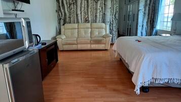 A hotel room with a wooden floor, a beige sofa, a bed with white bedding, a TV on a stand, and a wardrobe.