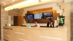 Un comptoir d’accueil dans le GreenTree Inn, avec un écran numérique au-dessus, deux réceptionnistes et une plante verte sur la droite.