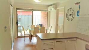 A modern kitchen with a central island, a dining area with chairs and a table, and a large wall clock.