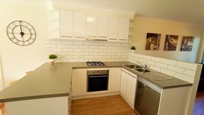 A compact kitchen with white cabinets, a gas stove, a dishwasher, and a sink.