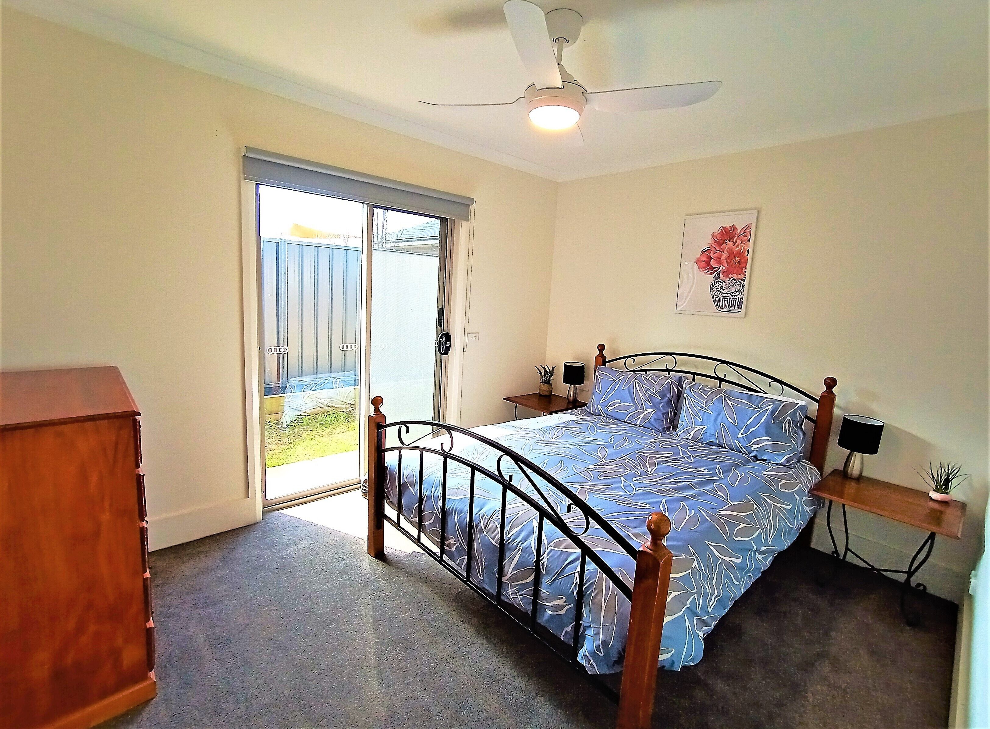 Quarto com cama, ventilador de teto, janela e porta que dá para área externa.