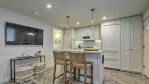 Una cocina moderna con armarios blancos, una isla central, taburetes de bar e iluminación colgante.