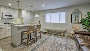 Una cocina moderna con armarios blancos, un microondas integrado y una zona de bar con dos taburetes.