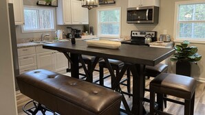 Una cocina moderna con armarios blancos, una isla central con taburetes, un microondas integrado y una lámpara colgante.