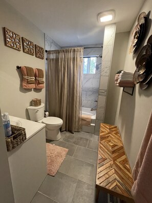 A bathroom with a toilet, sink, and shower area. There are towels hanging on the wall and a wooden shelf with towels.