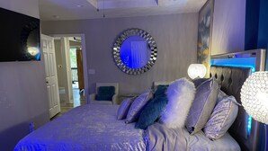 Un dormitorio moderno con una cama grande, un espejo redondo y una mesita de noche con lámpara.