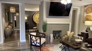 Una sala de estar moderna con chimenea, ventilador de techo y televisor de pantalla plana montado en la pared.