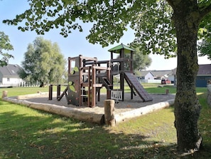 Une aire de jeux avec des structures d’escalade et un toboggan, entourée d’herbe et d’arbres.