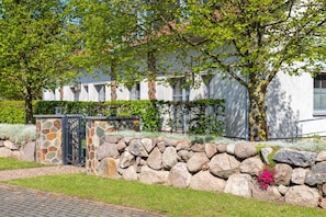 Un mur de pierre avec une porte, un chemin pavé et un bâtiment à la façade blanche et aux fenêtres.