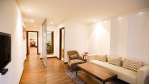 Un salón moderno con suelo de madera, un sofá con cojines estampados, una mesa de centro y un televisor montado en la pared.