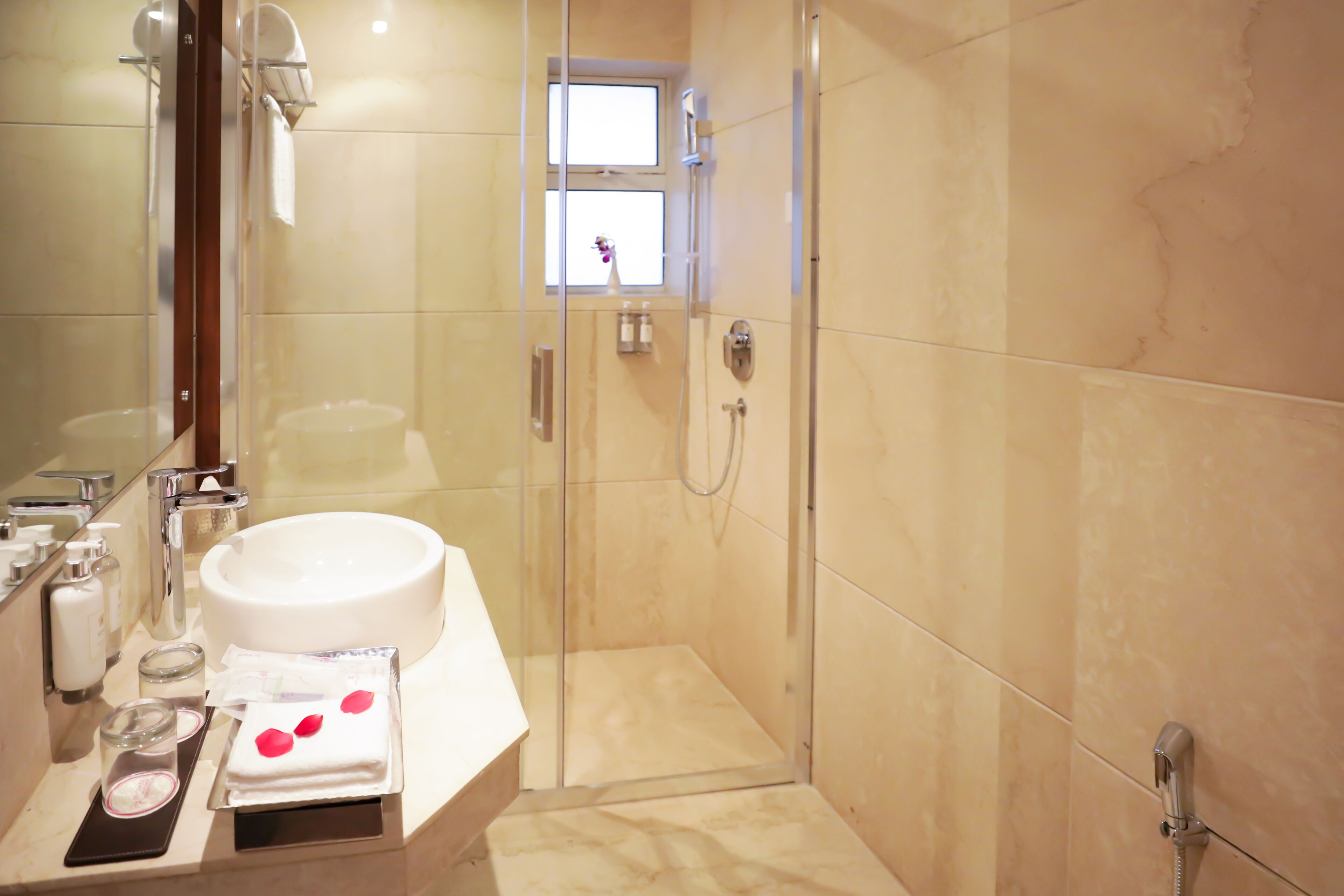 A modern bathroom with a large sink, glass shower enclosure, and a small window.