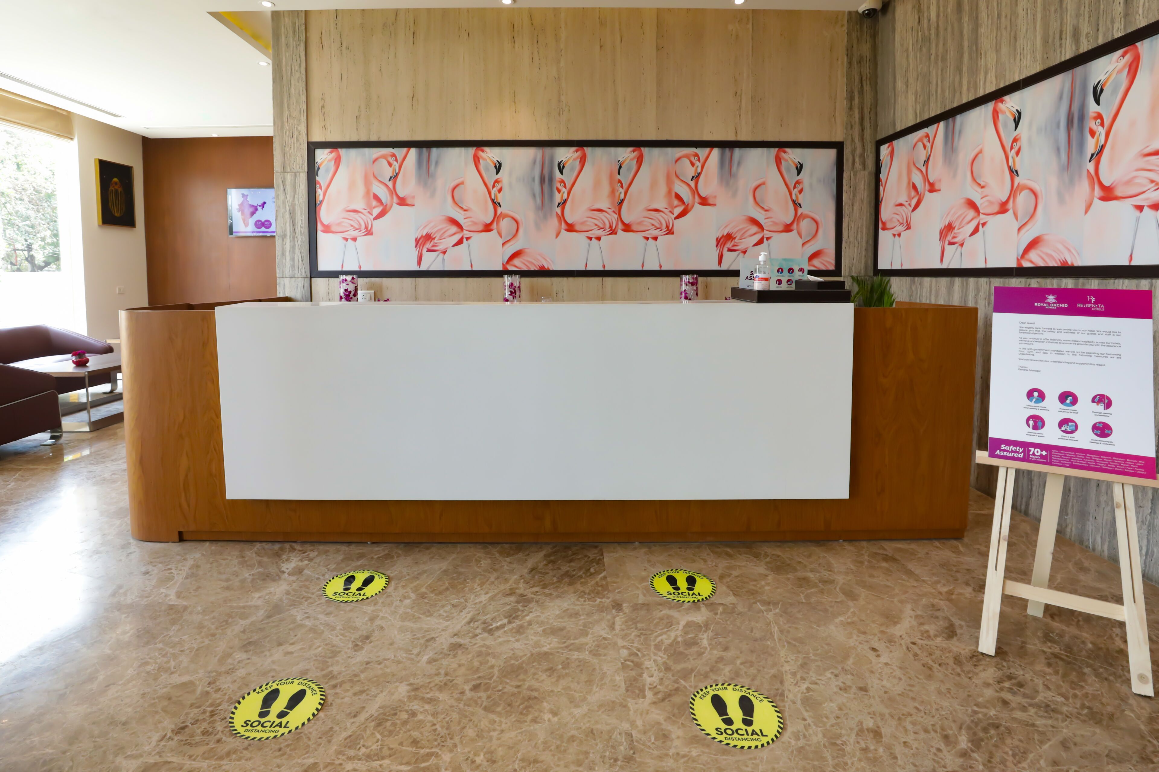 Ein Empfangsbereich mit einem Holzbüro, einem großen Flamingo-Gemälde an der Wand und einer Informationsstelle für Sicherheitsvorkehrungen.