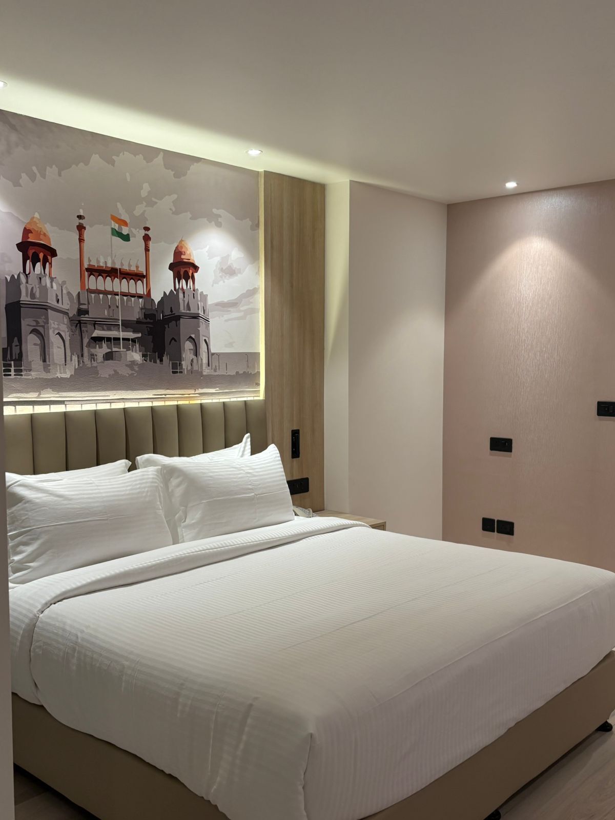 A modern hotel room with a large bed, a headboard with a mural, and a minimalist design.