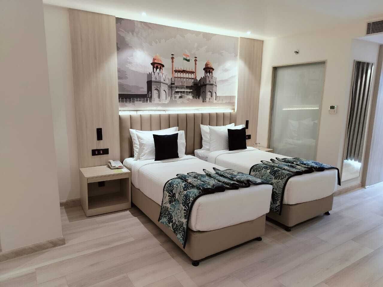Quarto de hotel com duas camas, uma mesa de cabeceira, um grande mural de um edifício histórico e uma porta de correr.