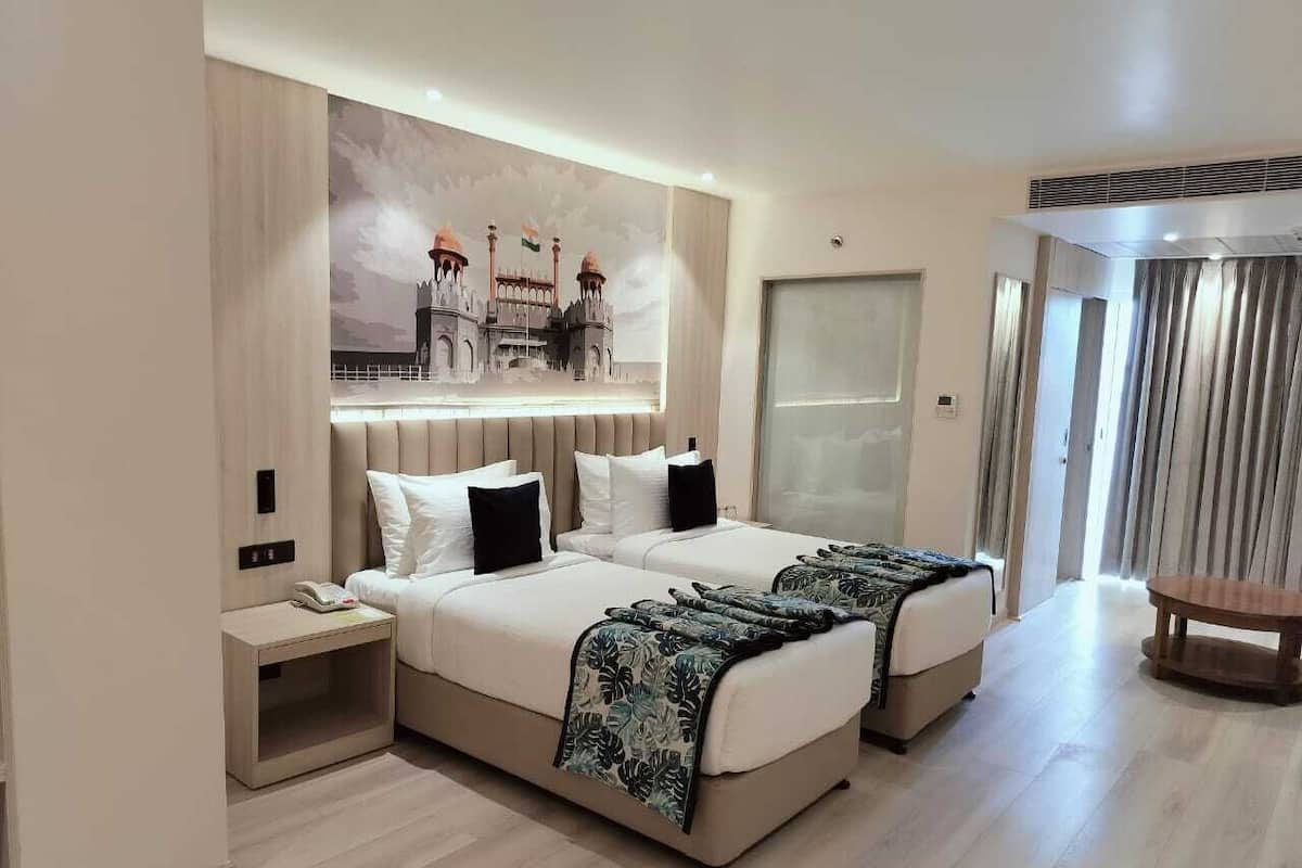 A hotel room with two beds, a bedside table, a small table, and a large window with curtains.