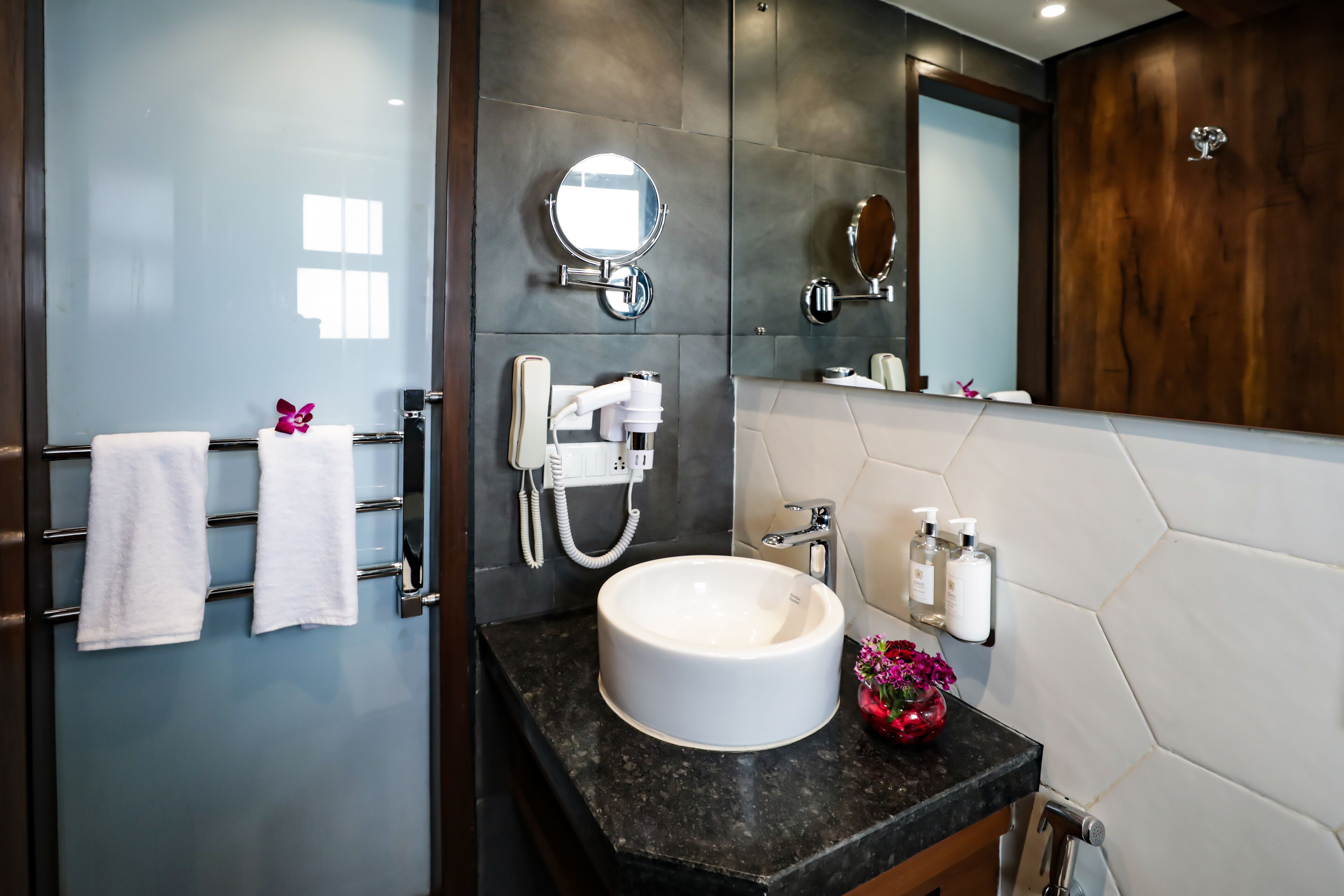 A modern bathroom with a large mirror, a round sink, and a towel rack with white towels.