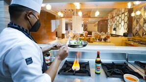 Un cocinero preparando comida en una estufa a gas, con una botella y un tazón de salsa sobre la encimera.