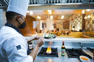 A chef cooking on a gas stove with a bottle of sauce and a bowl of sauce on the counter.