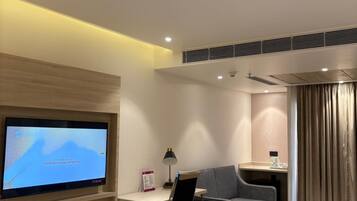 A modern hotel room with a flat-screen TV, a desk, a chair, a sofa, a small table, and a window with curtains.