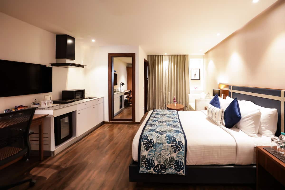 A hotel room with a bed, a desk, a TV, a kitchenette, and a bathroom.