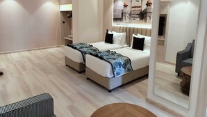 Una habitación de hotel moderna con dos camas, un espejo grande, una mesa redonda de madera y vistas a un edificio a través de la ventana.