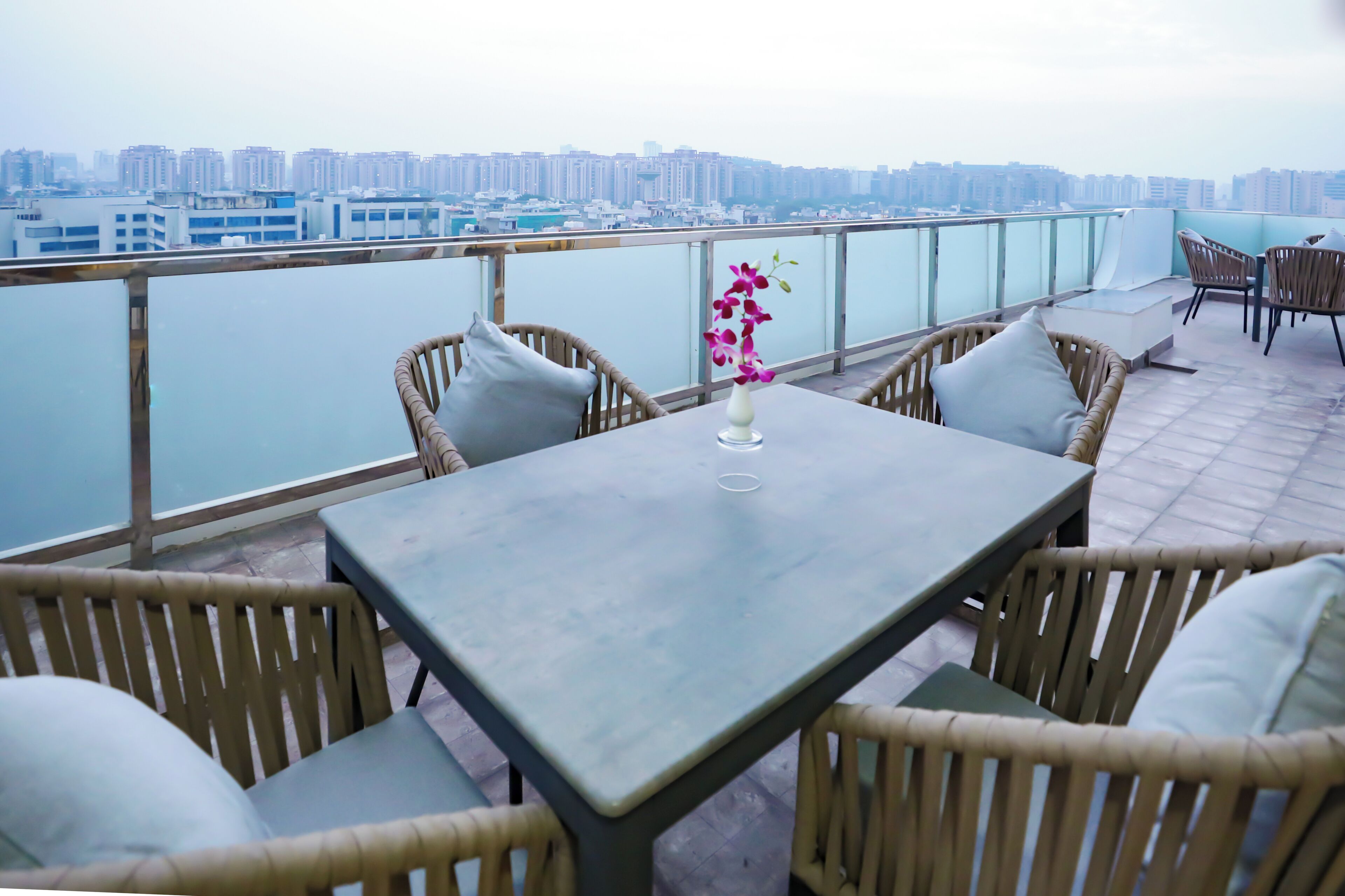 Eine Dachterrasse mit Tisch und Korbstühlen, mit Blick auf eine Stadtlandschaft.