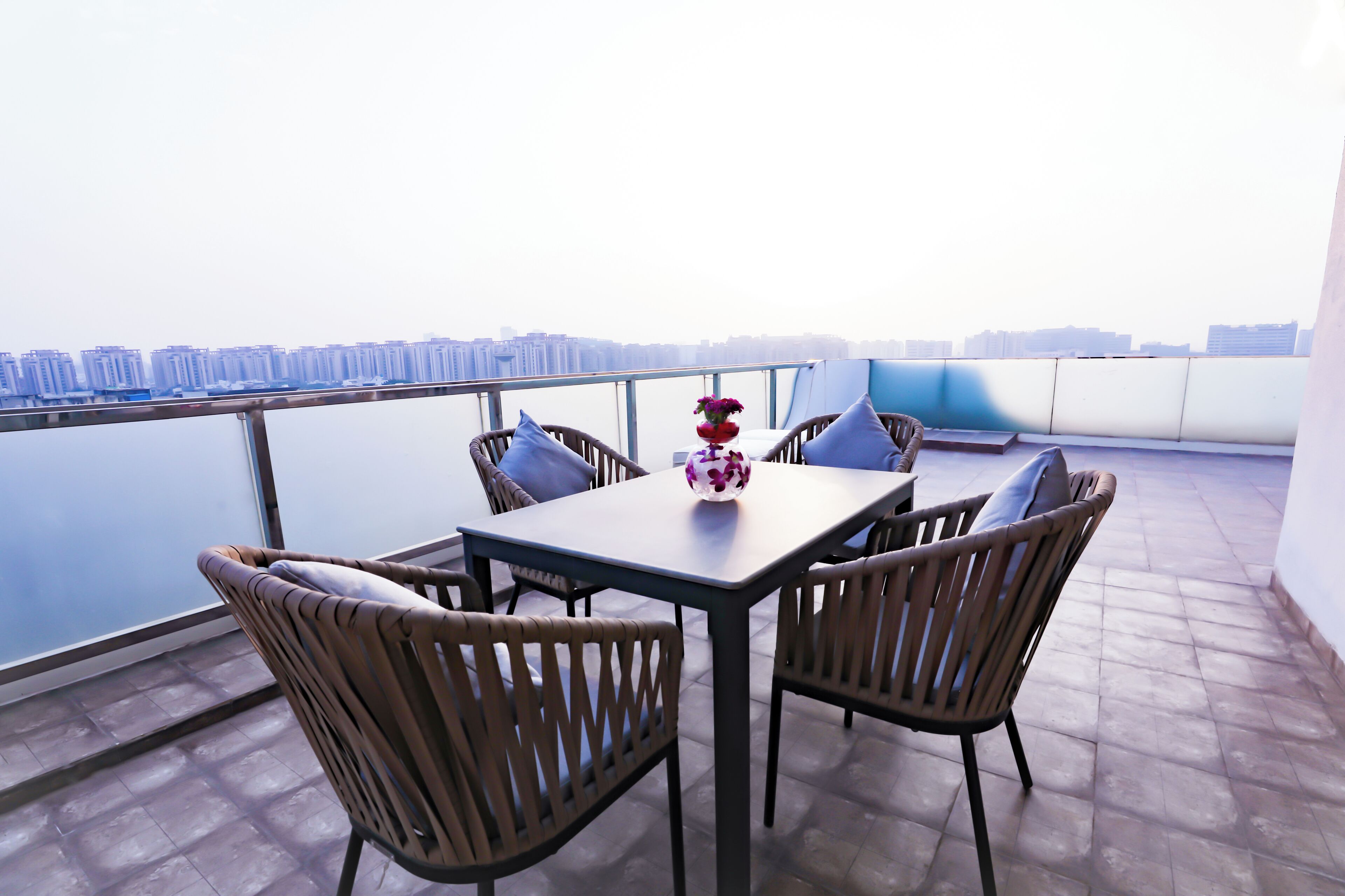Un balcon avec une table et des chaises, un vase rempli de fleurs et une vue sur la ville.