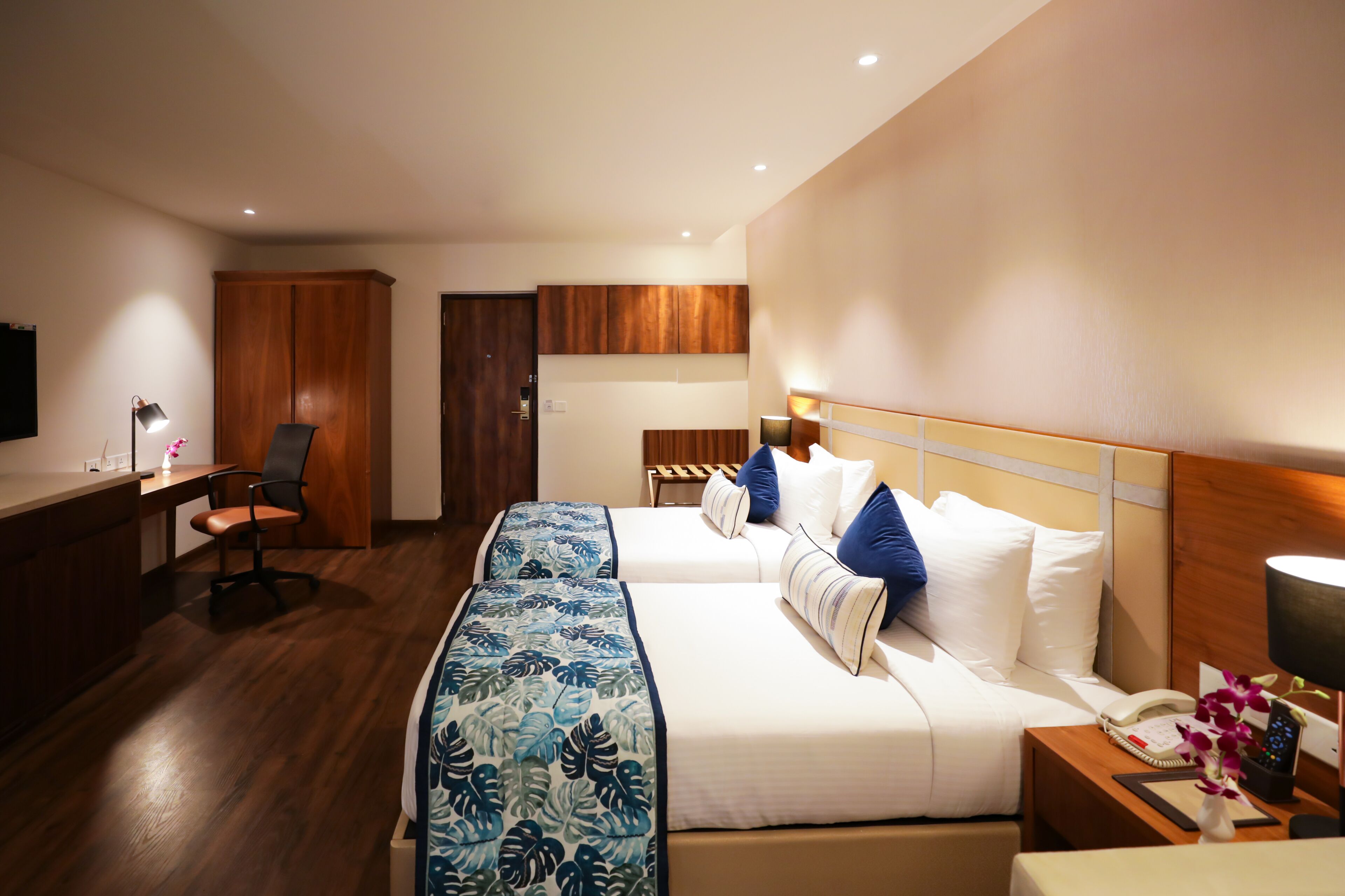 A hotel room with a bed, bedside table, desk, chair, and a TV.