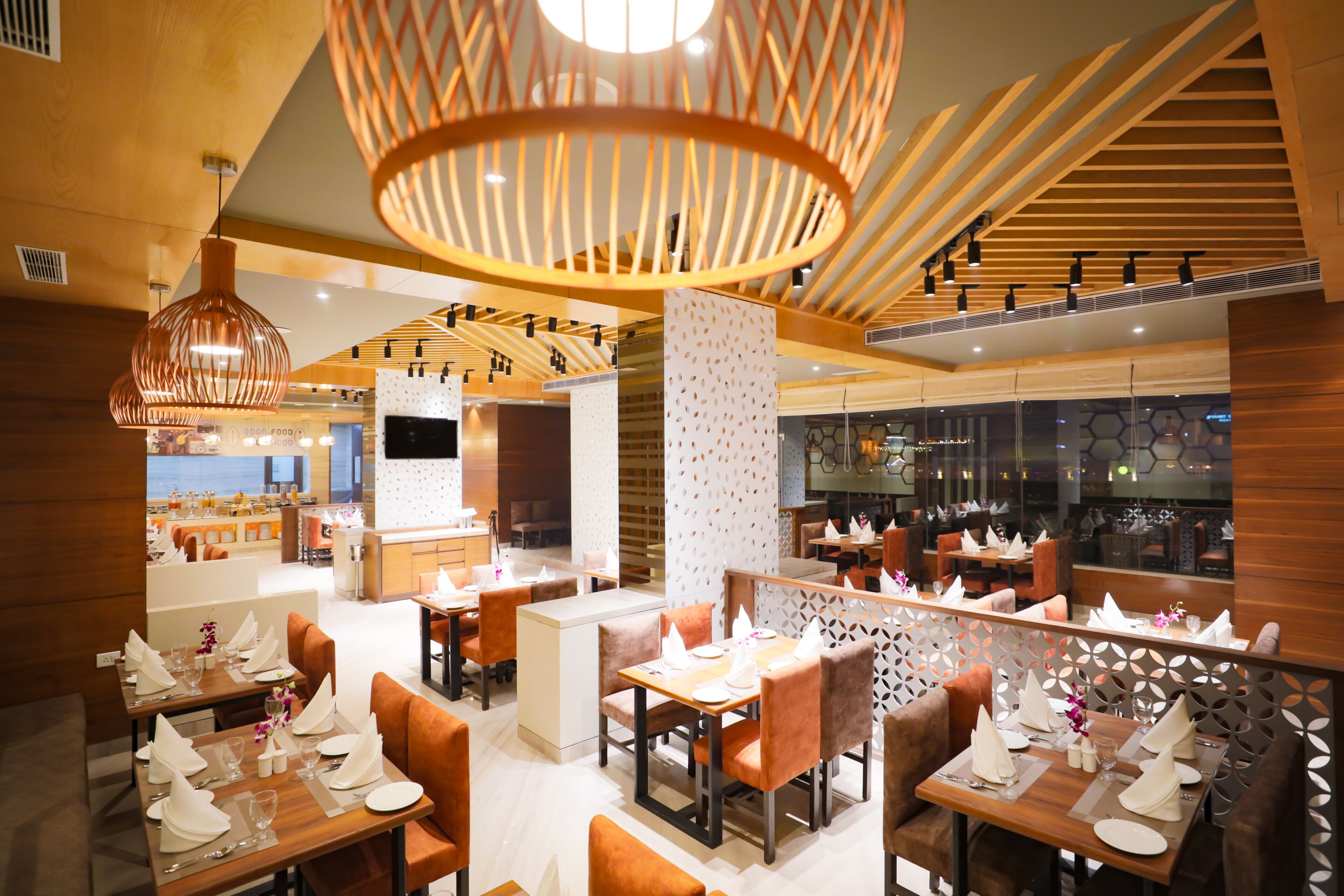 Un interior de restaurante moderno con detalles de madera, varias zonas de comedor y vistas a la cocina.