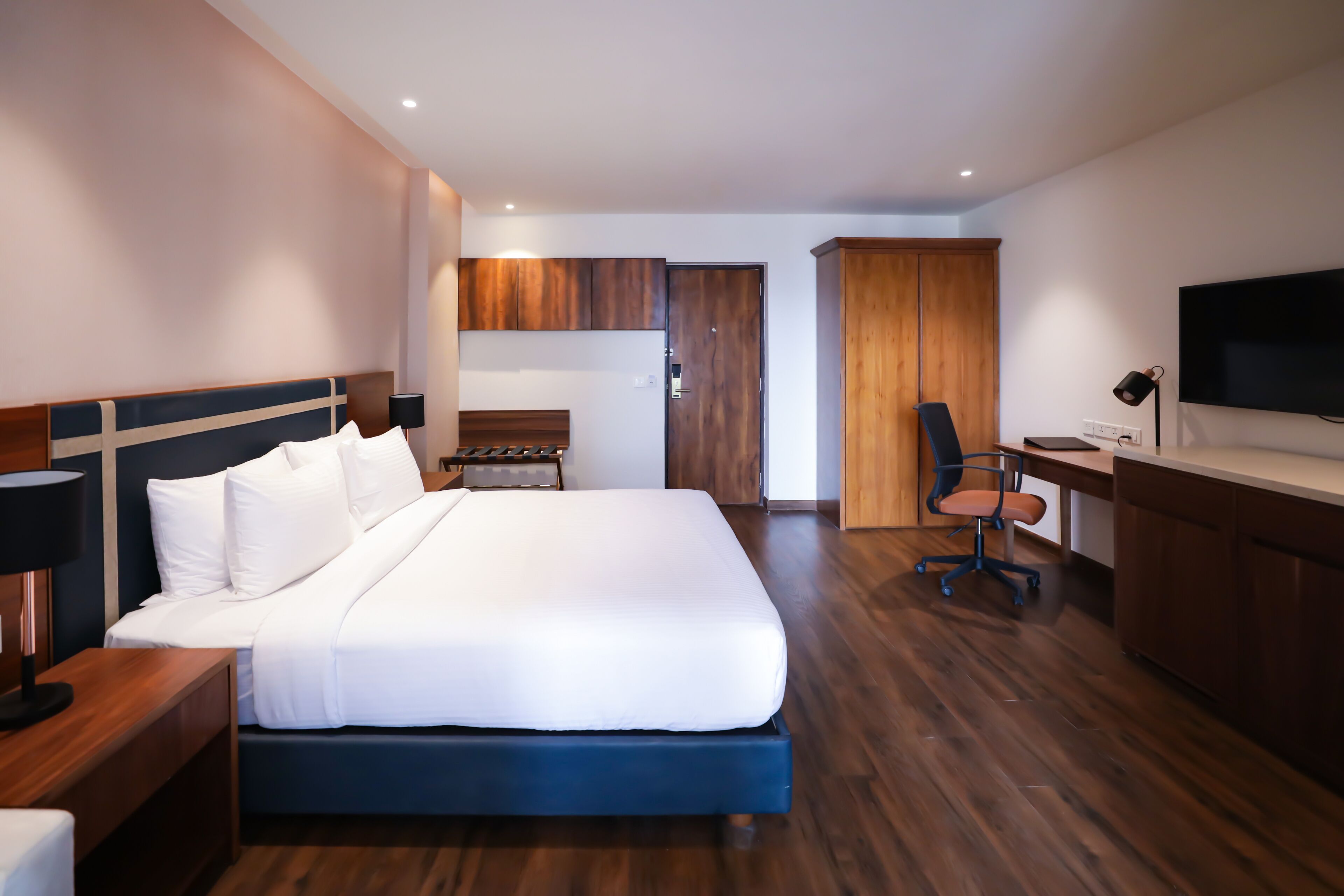 Una habitación de hotel moderna con una cama grande, un escritorio, una silla, un televisor y suelo de madera.