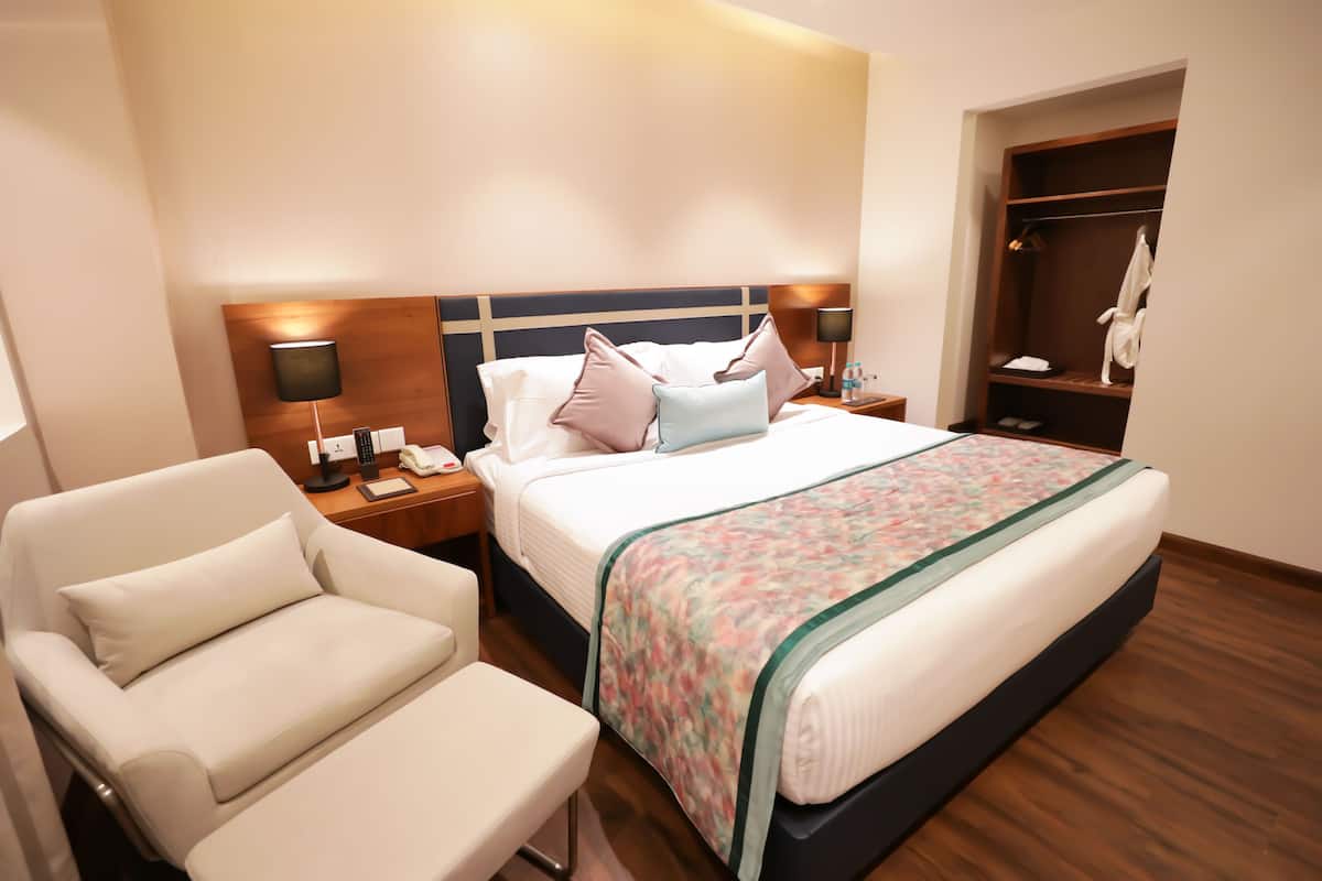 A hotel room with a bed, bedside tables, a chair, a wardrobe, and a mirror.