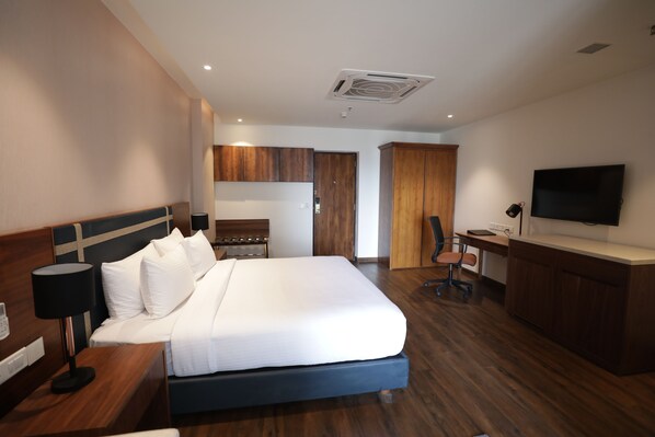 A hotel room with a large bed, a desk, a chair, a television, and wooden cabinets.