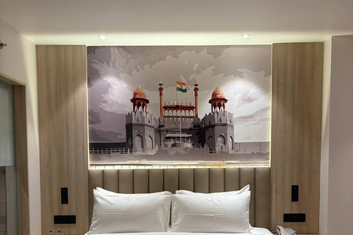 A hotel room with a large bed, a wall-mounted artwork of a historical building, and bedside tables with lamps.