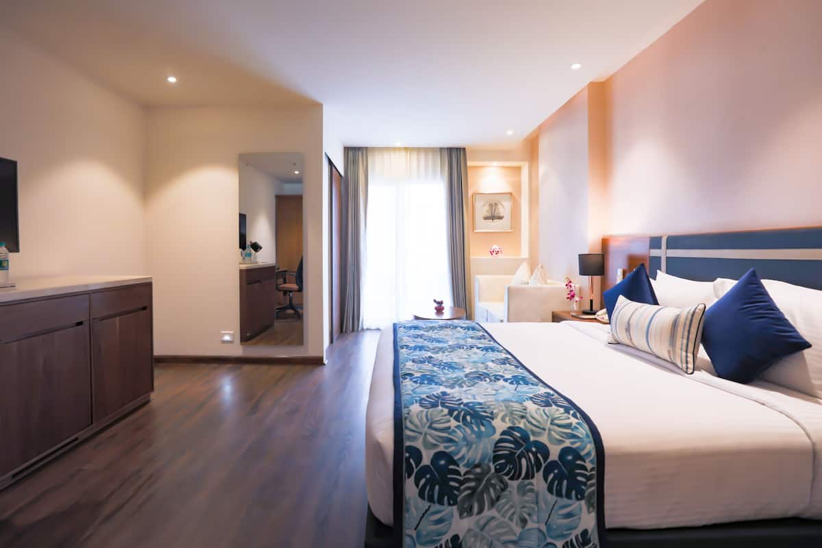 A hotel room with a large bed, a wooden desk, and a view of the hallway.