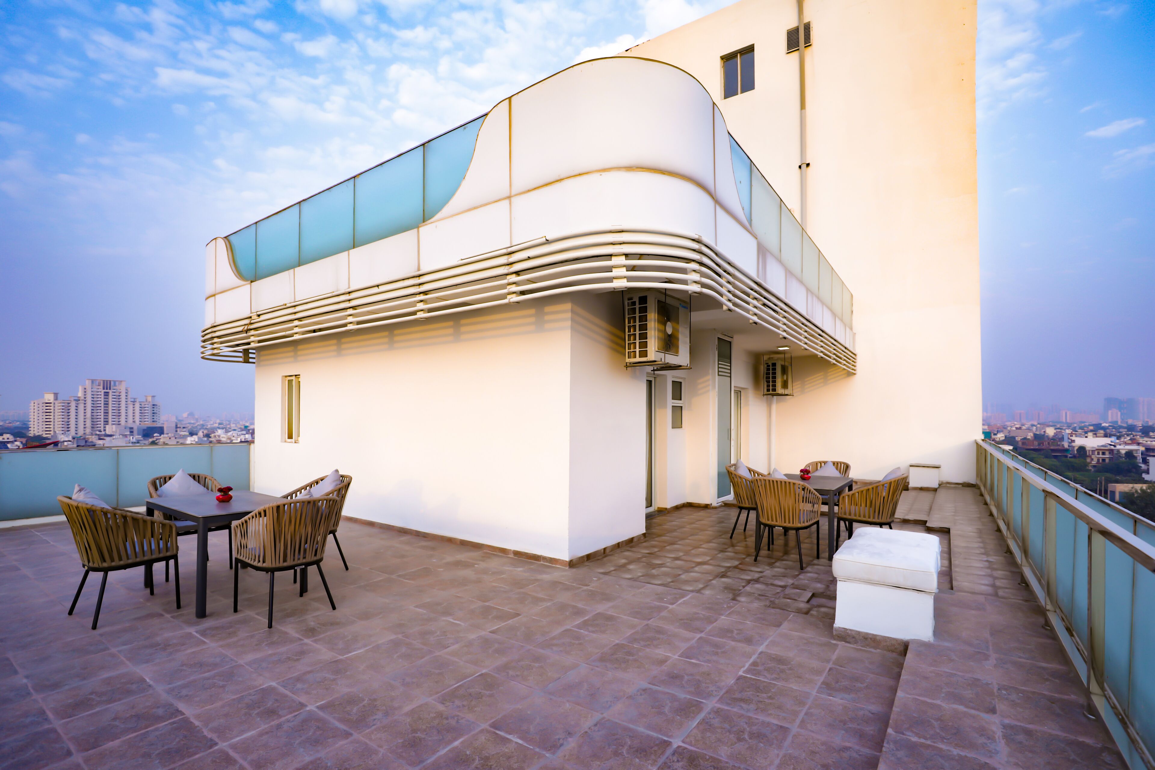 A modern building with a curved balcony, outdoor seating, and a city view.