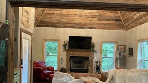 A cozy cabin interior with a fireplace, wooden walls, a red sofa, and a television. - RUSTIC GLAM (Mentone)