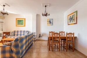 A living room with a sofa, a dining table with chairs, a chandelier, and framed artwork on the walls. - Apartment 'Luxury CARABEO 2000 2-1' with Pool, Garden, Wi-Fi & A/C (Nerja)