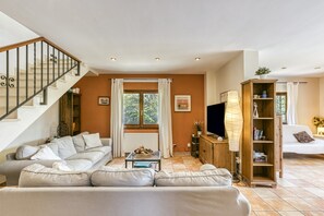 A living room with a staircase, a sofa set, a TV, a wooden cabinet, and a window with curtains.