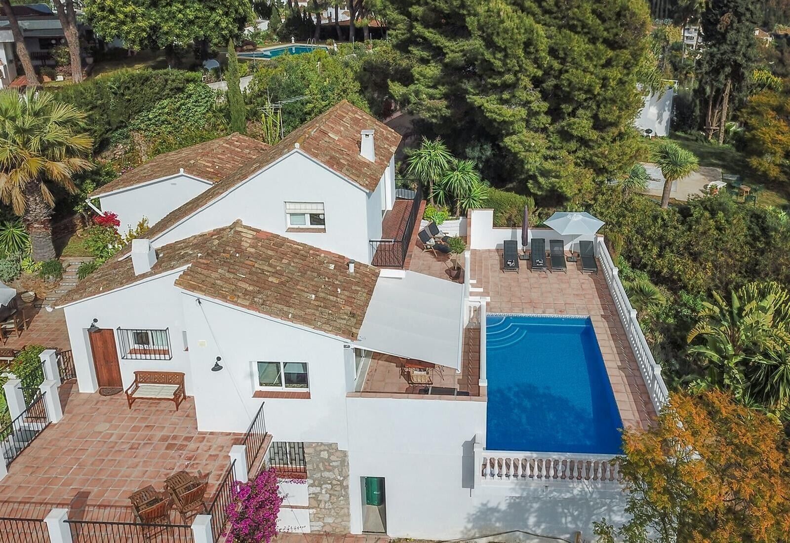 Una villa blanca con piscina, un patio con sillas y vistas a la vegetación circundante.