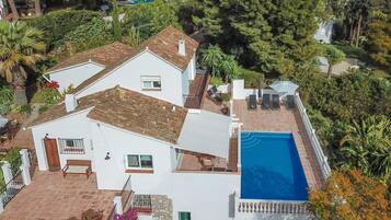 Una villa blanca con piscina, un patio con sillas y vistas a la vegetación circundante.