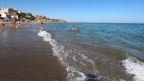 Une plage avec des gens, un ciel dégagé et des bâtiments en arrière-plan.