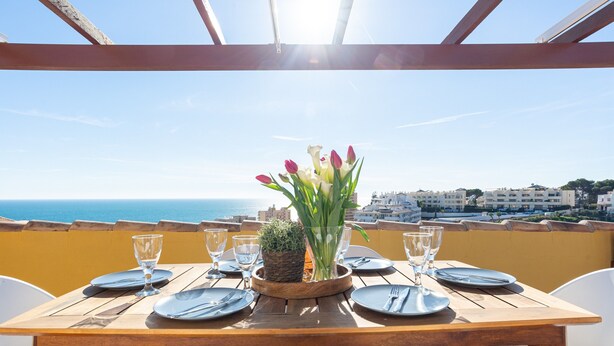 Une table dressée pour le dîner, avec vue sur la mer et des bâtiments en arrière-plan.