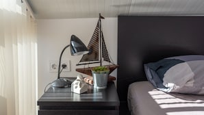 Une chambre à coucher bien rangée, avec un lit, une table de chevet dotée d’une lampe, une petite plante et un objet décoratif.