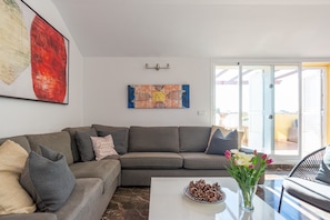 Een moderne woonkamer met een modulaire bank, een bijzettafel met dennenappels, een vaas met bloemen en kunstwerken aan de wanden.