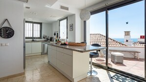 Een moderne keuken met een groot schiereiland, een eethoek met uitzicht en een balkon met uitzicht op zee.