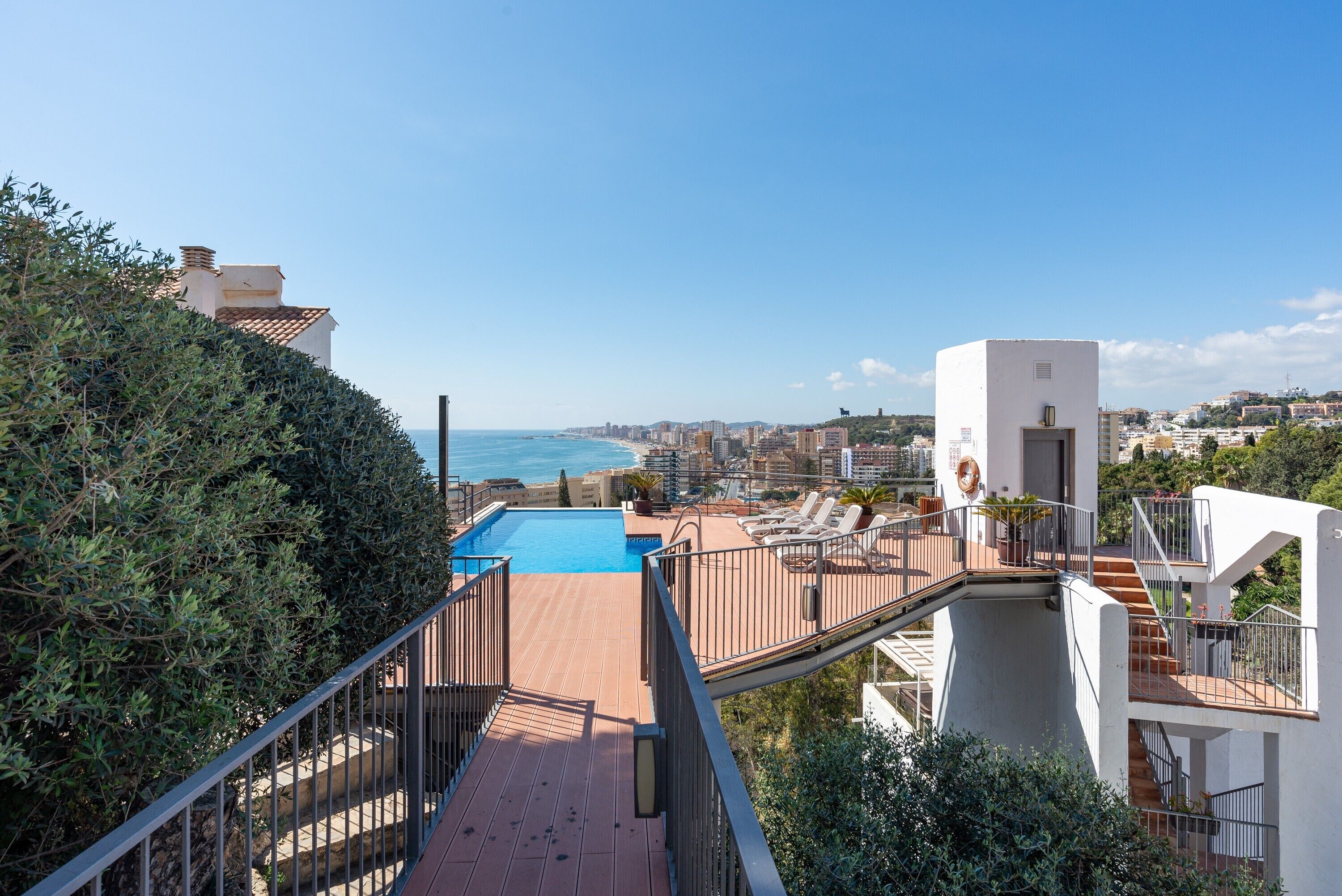 Une piscine sur le toit avec vue sur la mer, un bâtiment blanc et un escalier.