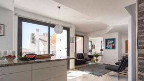 Een moderne keuken met een groot raam, een eethoek met een zwarte bank en een woonkamer met een zwarte stoel.
