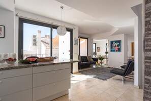 A modern kitchen with a large window, a dining area with a black sofa, and a living room with a black chair. - Holiday Home 'Modern Townhouse with Stunning View' with Sea View, Wi-Fi and Air Conditioning (Fuengirola)