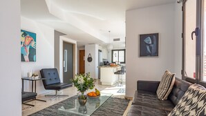 Een moderne woonkamer met een glazen salontafel, een bank en een eethoek op de achtergrond.