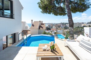 Una piscina sul tetto con vista sulla città, un tavolo di legno con bottiglie e un divano bianco.